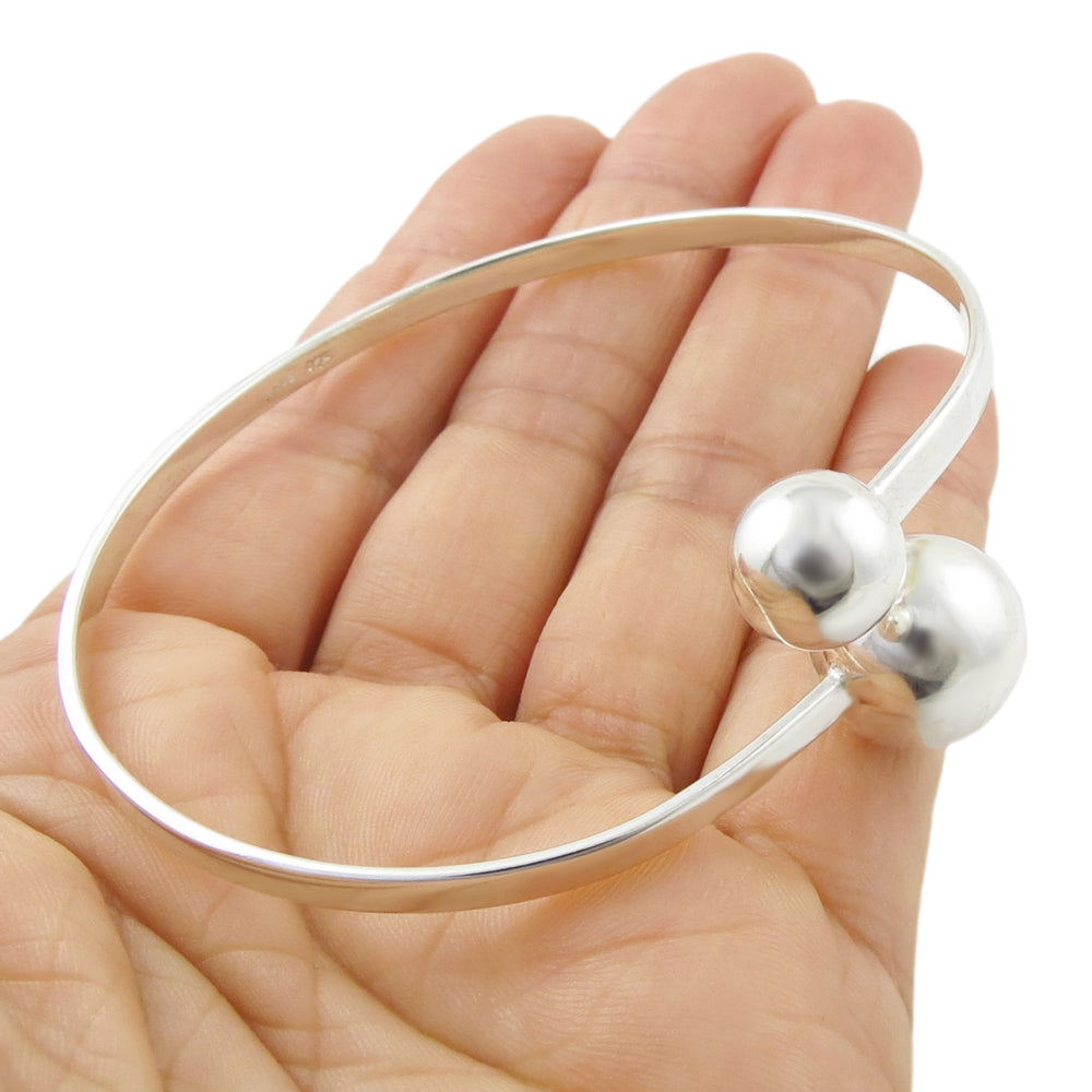 Silver bangle with two silver beads held in a hand against a white background