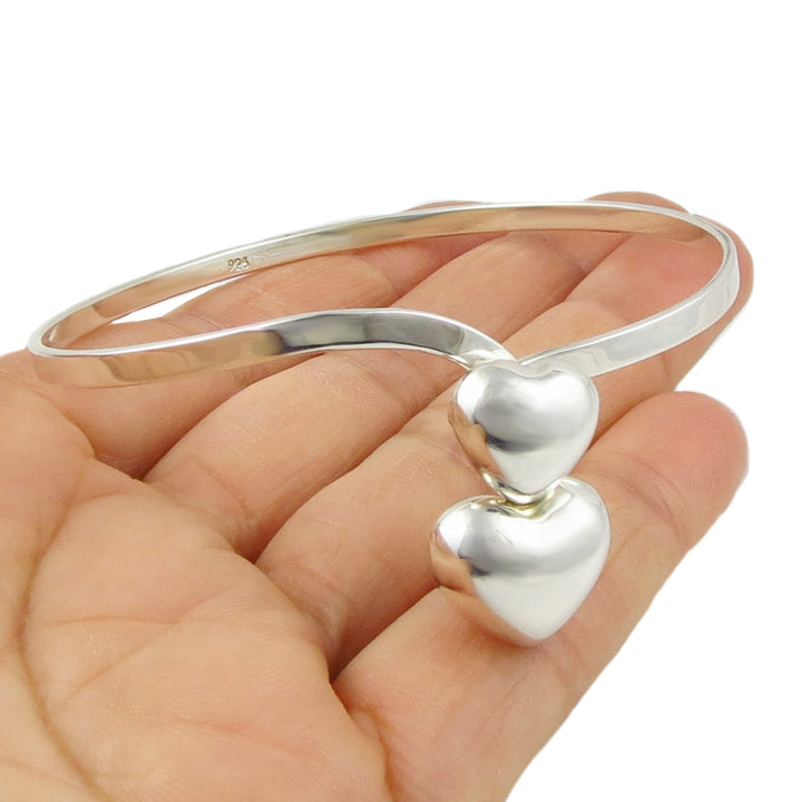 925 silver bangle with heart-shaped ends held in a hand on a white background