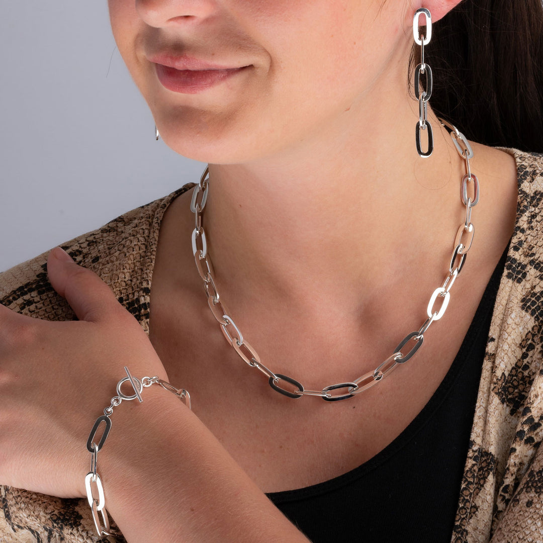 Chunky sterling silver chain link necklace, earrings and matching bracelet worn by a woman in a brown and black top