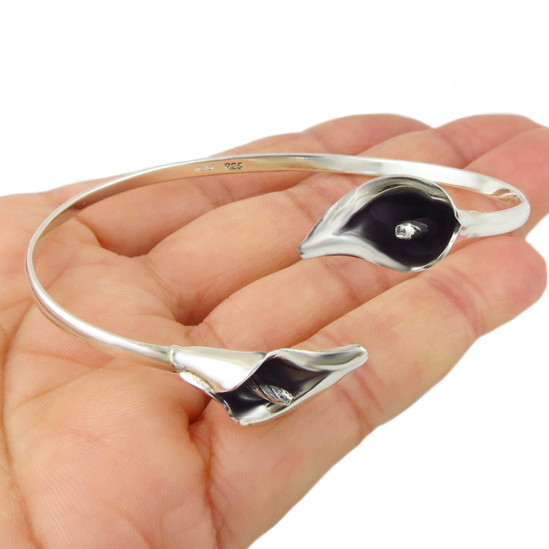 Silver bracelet with calla lily flower accents held in a hand on a white background