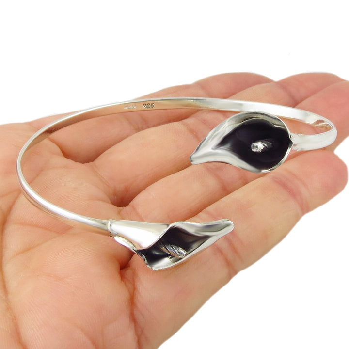 Silver bracelet with calla lily flower accents held in a hand on a white background