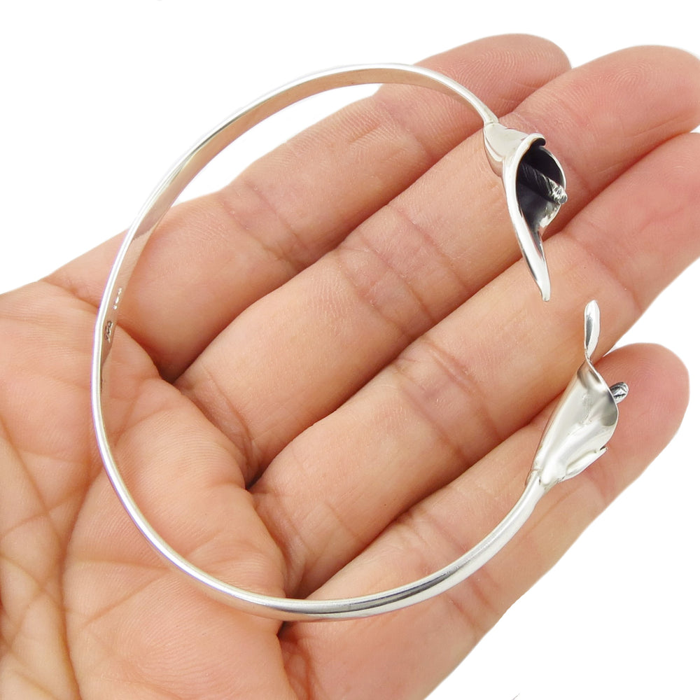 A sterling silver bracelet decorated with calla lily flowers held in a person's hand on a white background. 