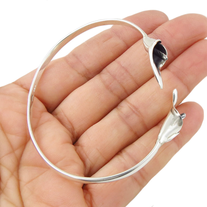 A sterling silver bracelet decorated with calla lily flowers held in a person's hand on a white background. 
