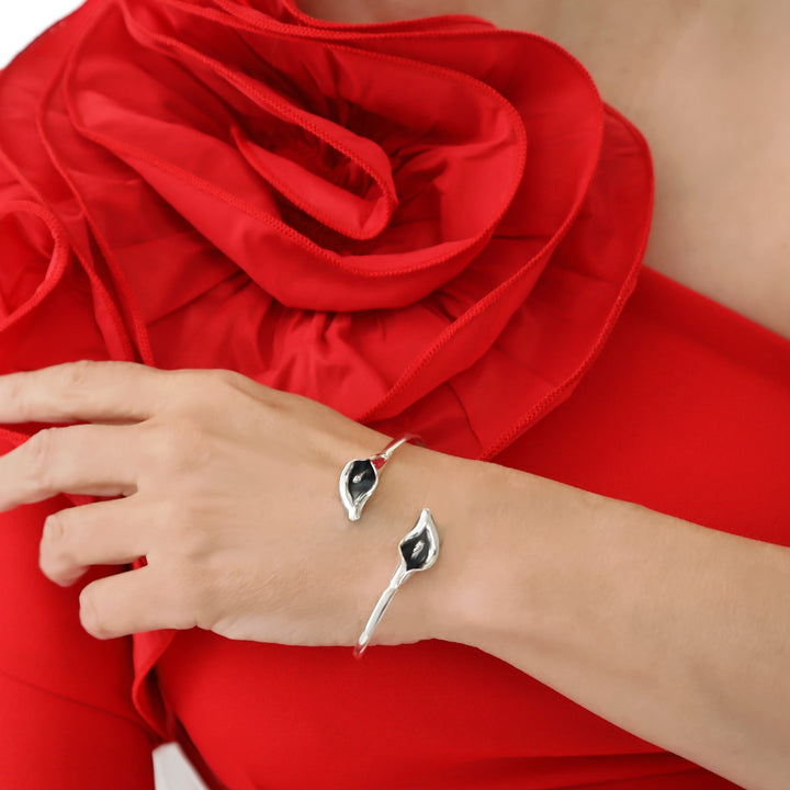 A woman wearing a red dress with a large frill and a sterling silver bracelet decorated with calla lily flower accents. 