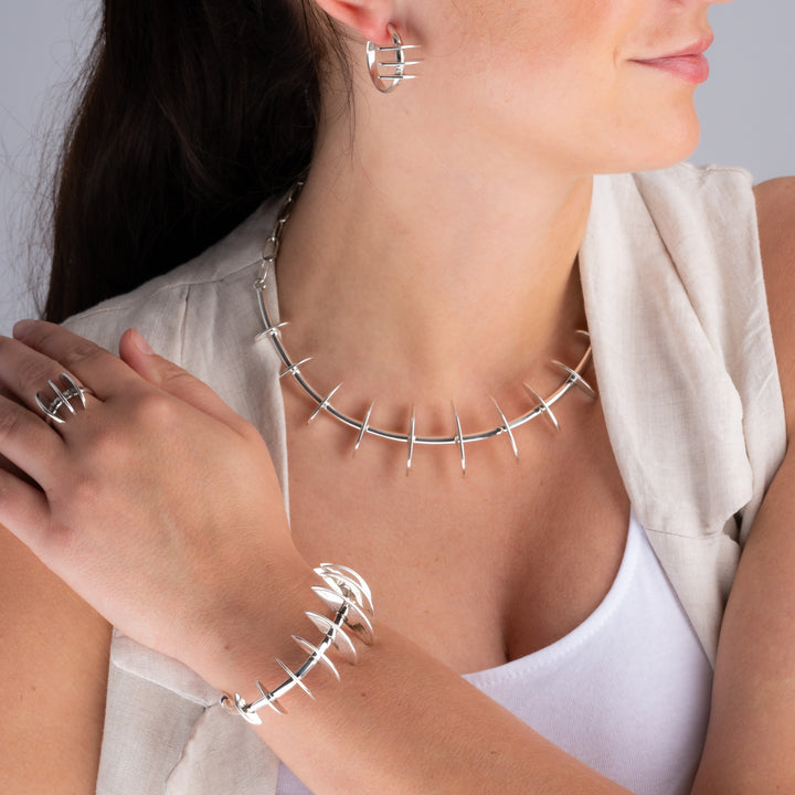 A close-up of a model wearing a Mexican designer 925 silver jewellery set featuring a curved necklace with spikes, a matching ring, hoop earrings and a matching cuff bracelet.