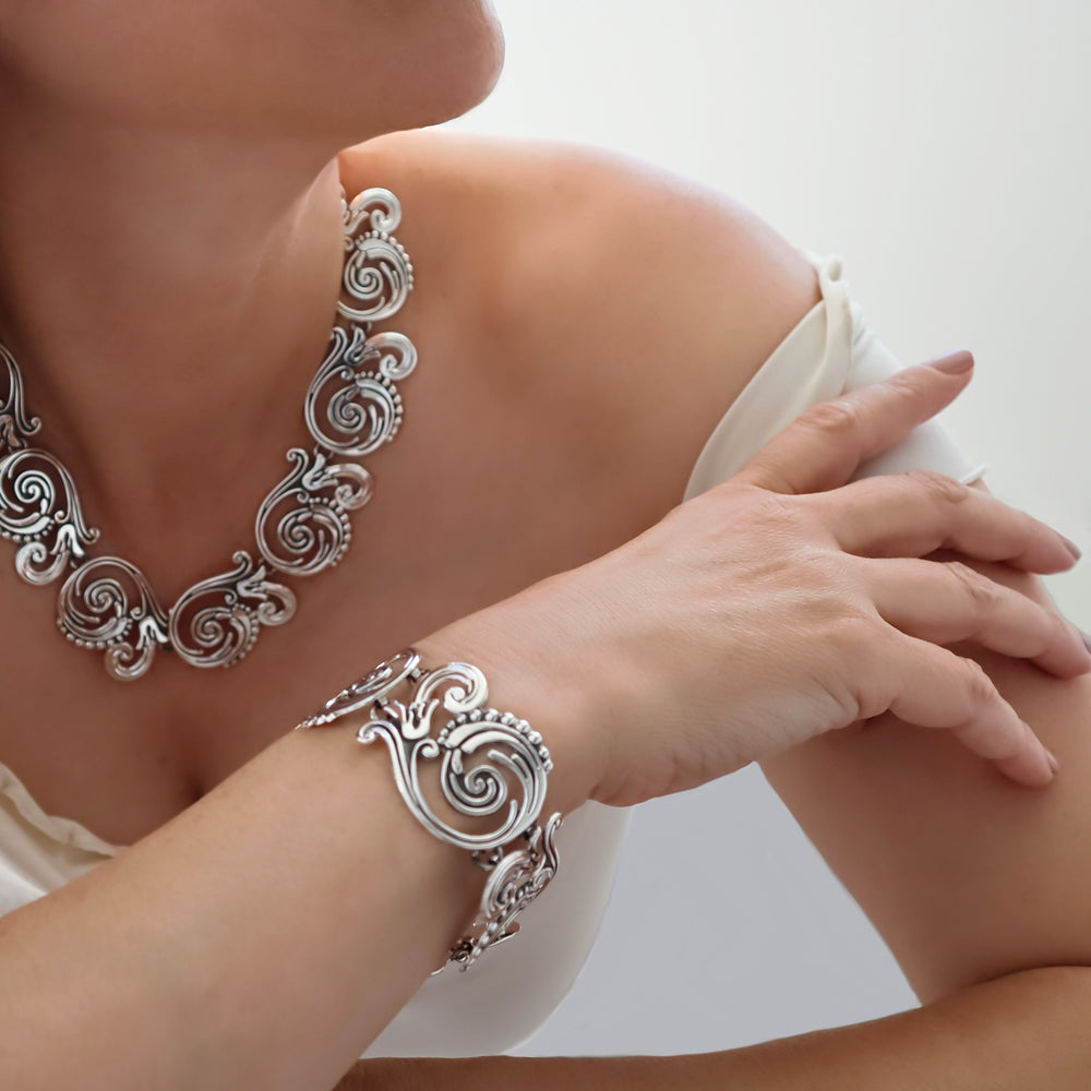 A close-up image of a woman wearing a detailed mexican 925 sterling silver necklace and matching bracelet with vine and flower-shaped links, showcasing a polished and antiqued blackened niello finish.