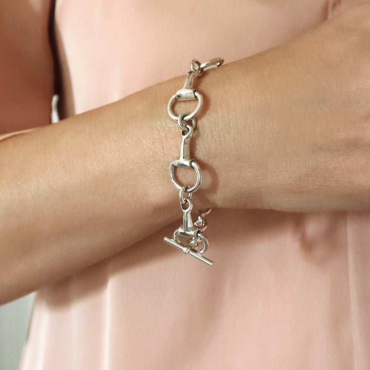 A woman wearing a long UK 925 sterling silver horse snafflebit bracelet with a polished finish and a t-bar toggle fastener
