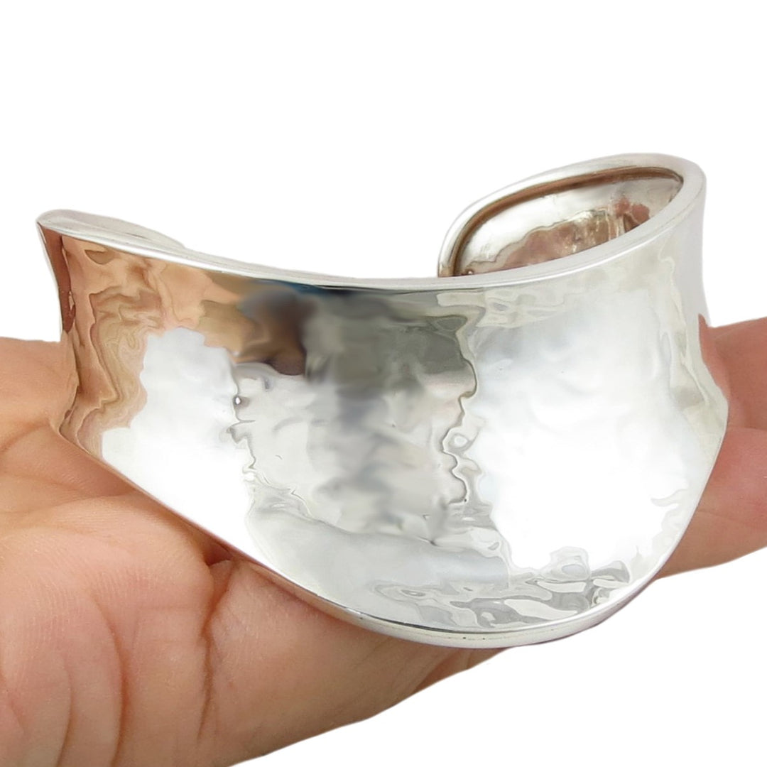 A wide sculpted sterling 925 silver bracelet cuff with a hammered finish held in a person's hand on a plain background. 