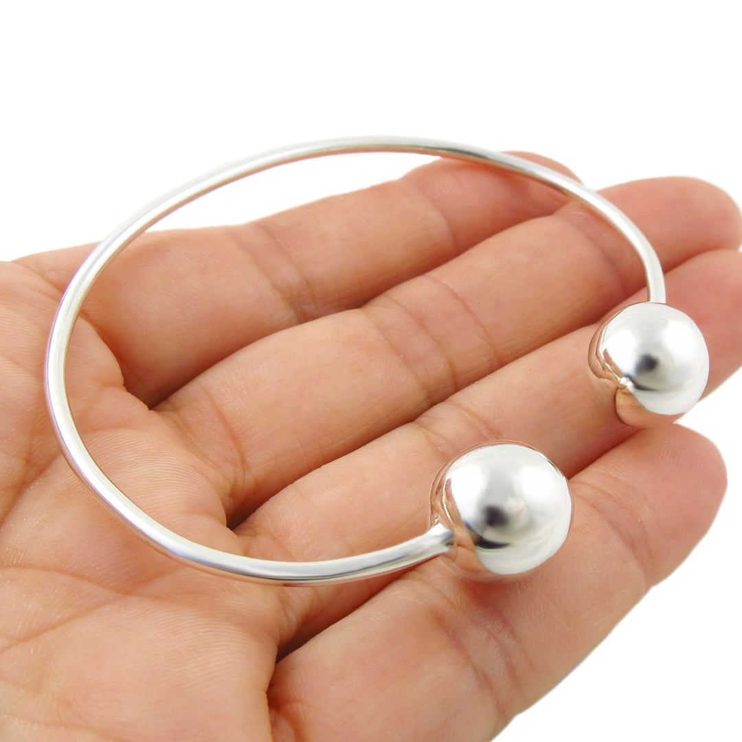 A Mexican 925 sterling silver open cuff bangle bracelet with two polished spherical ball bead accents on the ends, shown resting on a person's hand against a white background.
