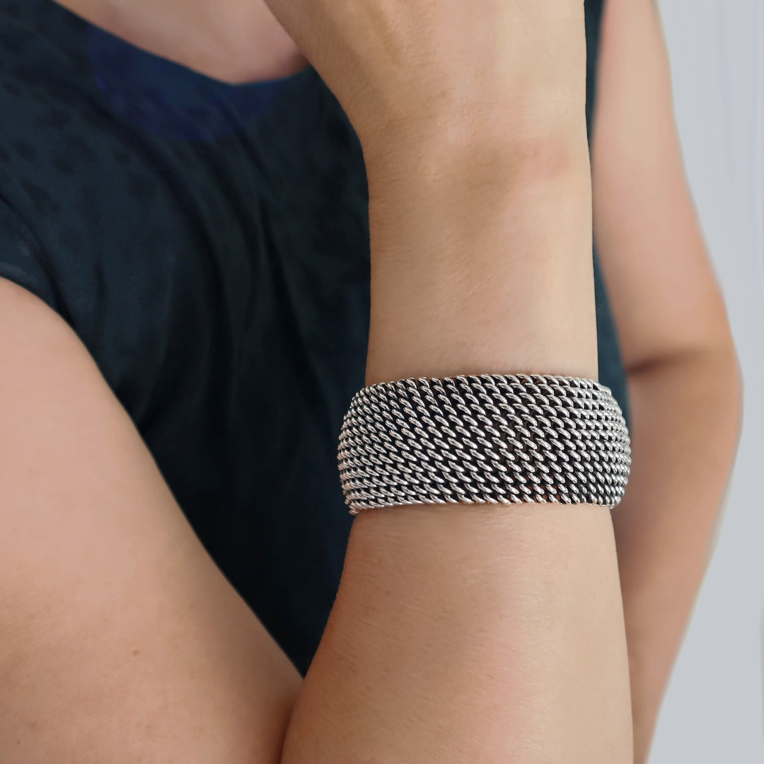 Woven chain sterling silver bracelet on a person's wrist with a neutral background
