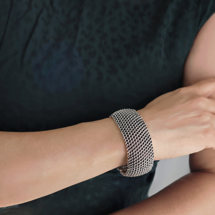 Person wearing a silver mesh bracelet on a dark background
