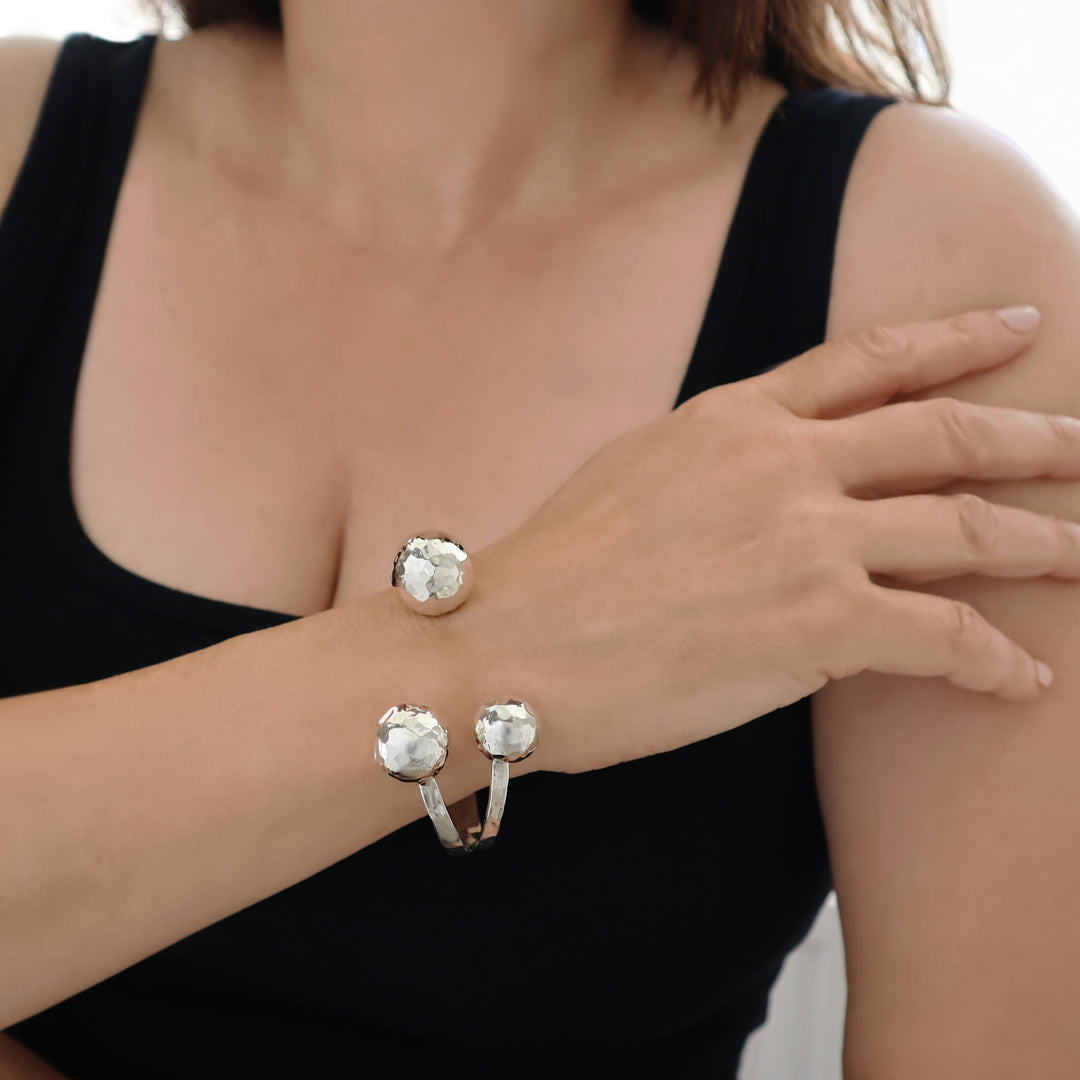 A large triple ball bead modern cuff style bracelet in UK hallmarked sterling silver with a hammered finish worn by a woman in a black vest
