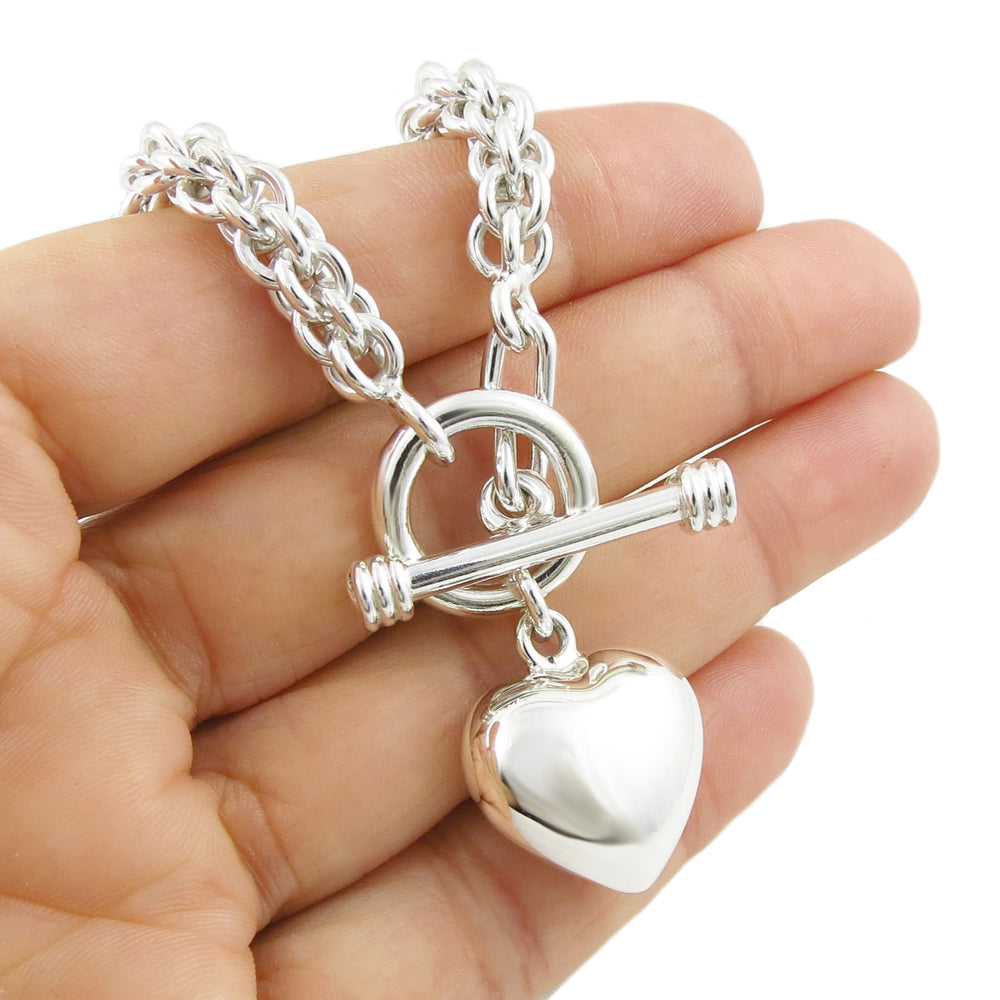 A large chunky UK hallmarked puffy love heart charm on a triple link chain bracelet held in a person's hand