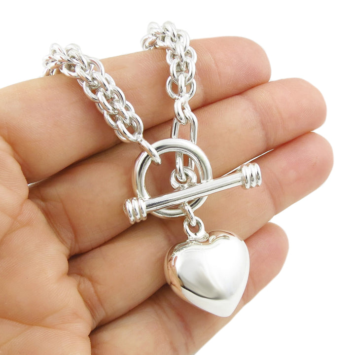A large chunky UK hallmarked puffy love heart charm on a triple link chain bracelet held in a person's hand
