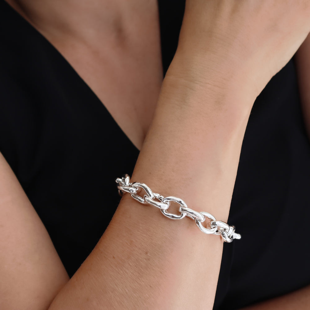 Chunky silver chain bracelet on a wrist against a black background