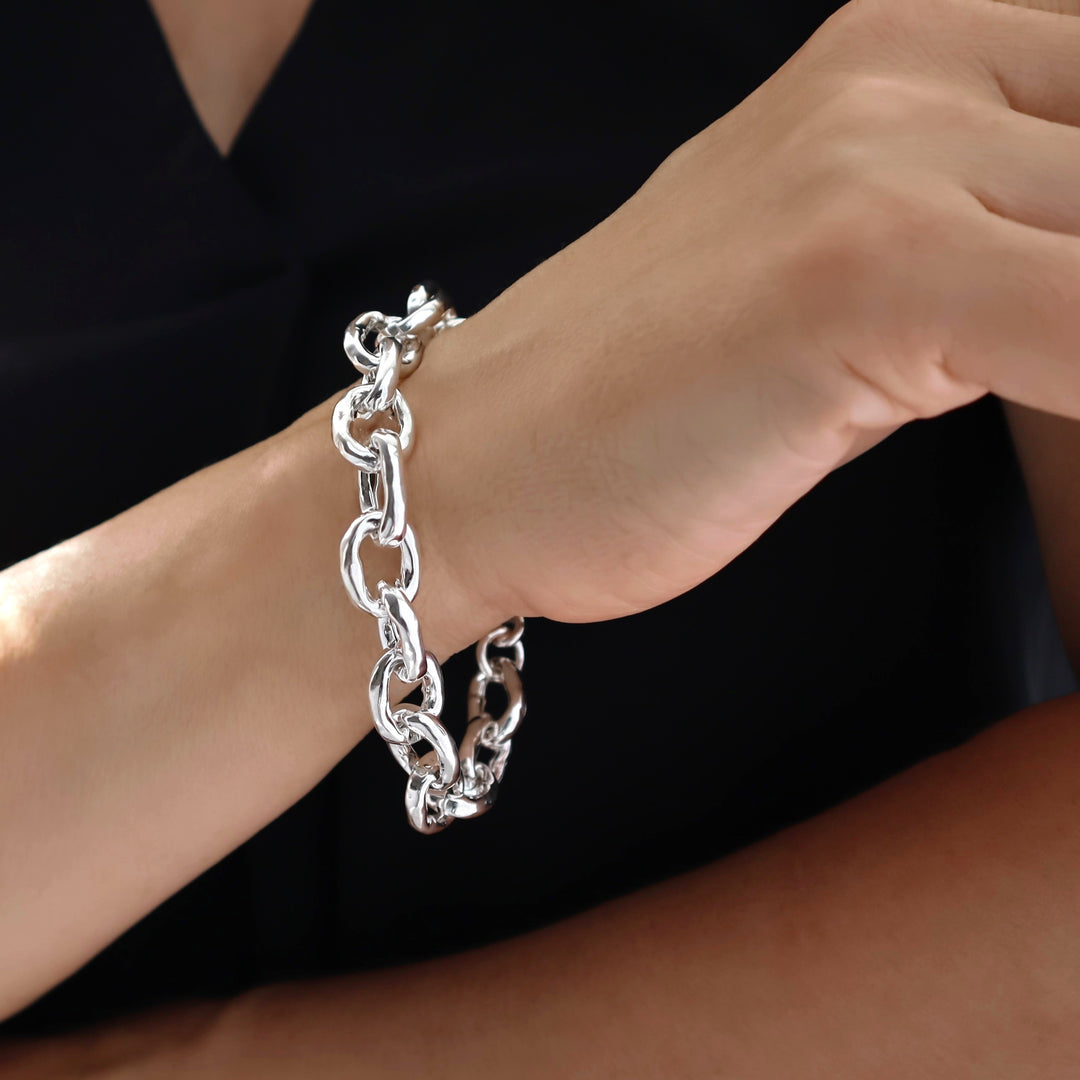 A person wearing a large hammered oval link chunky silver chain bracelet on their wrist. 