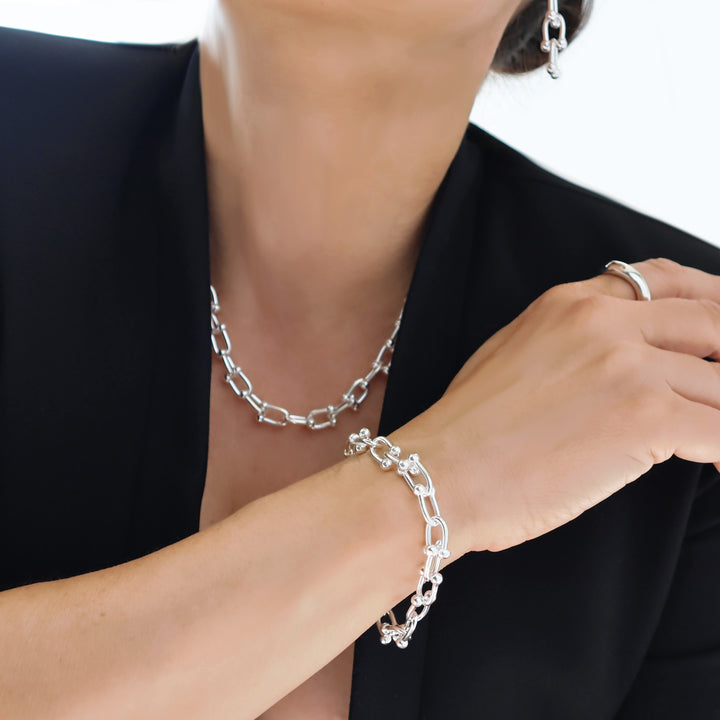 Silver gauge link chain bracelet and necklace and earrings on a person wearing a black outfit.