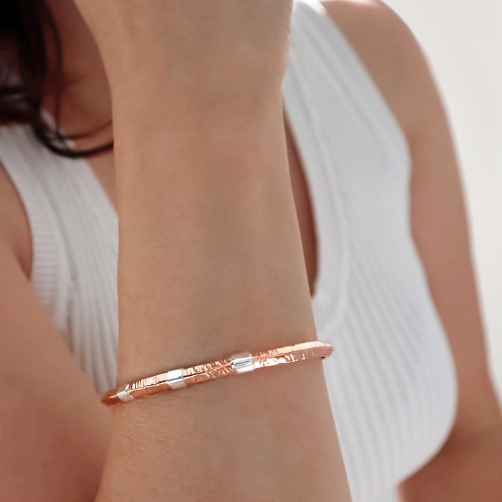 Copper bracelet with silver accents on a wrist with a blurred background. 