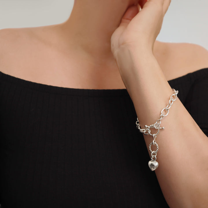 UK sterling 925 silver bracelet with a dangling hammered puffy heart charm on a woman wearing a black top.