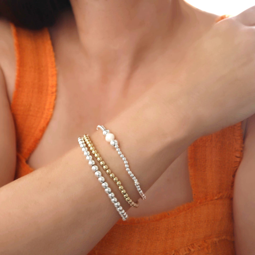 Close-up of a woman in an orange top wearing three beaded bracelets in a wrist stack