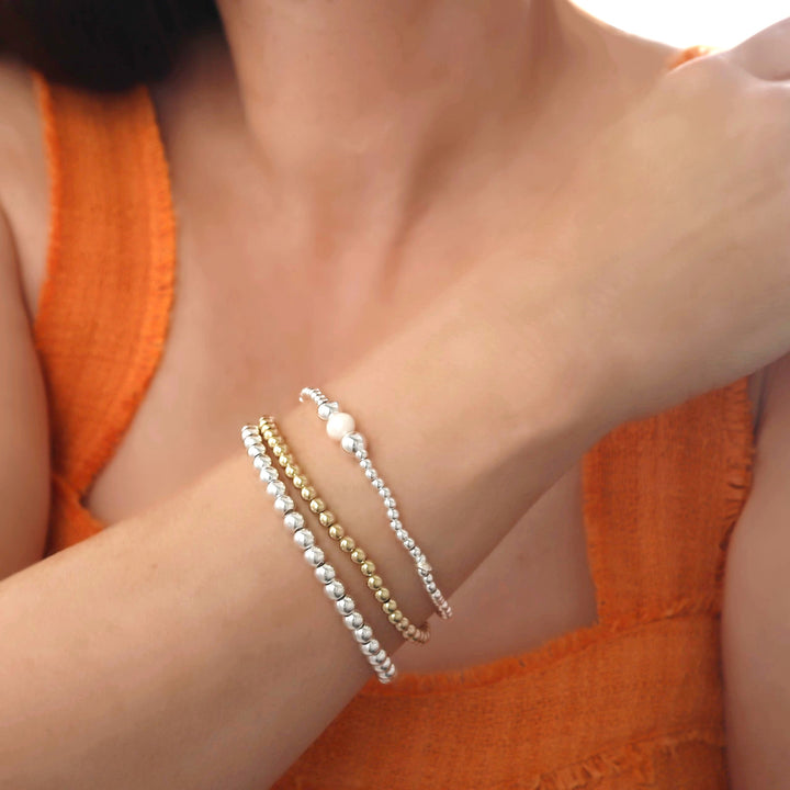 Close-up of a woman in an orange top wearing three beaded bracelets in a wrist stack