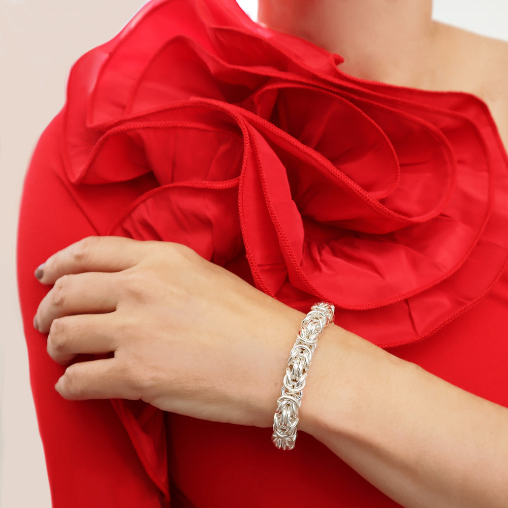 Chunky sterling 925 Silver byzntine chain bracelet on a woman's wrist with a red floral garment in the background
