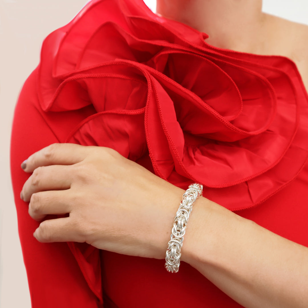 Chunky sterling 925 Silver byzntine chain bracelet on a woman's wrist with a red floral garment in the background