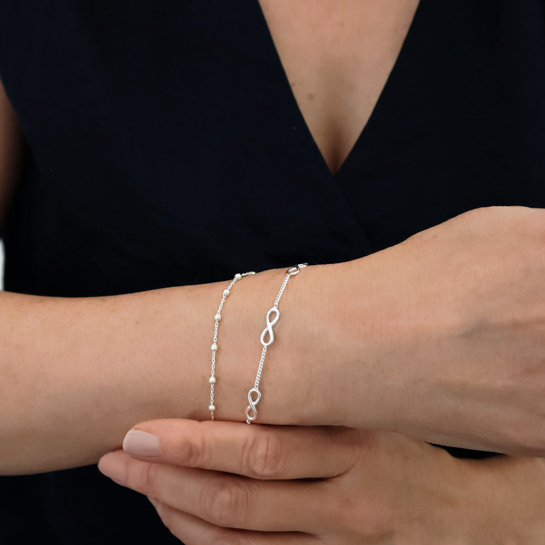 Close-up of a woman's wrist wearing two 925 silver chain bracelet wrisst stack on a black background