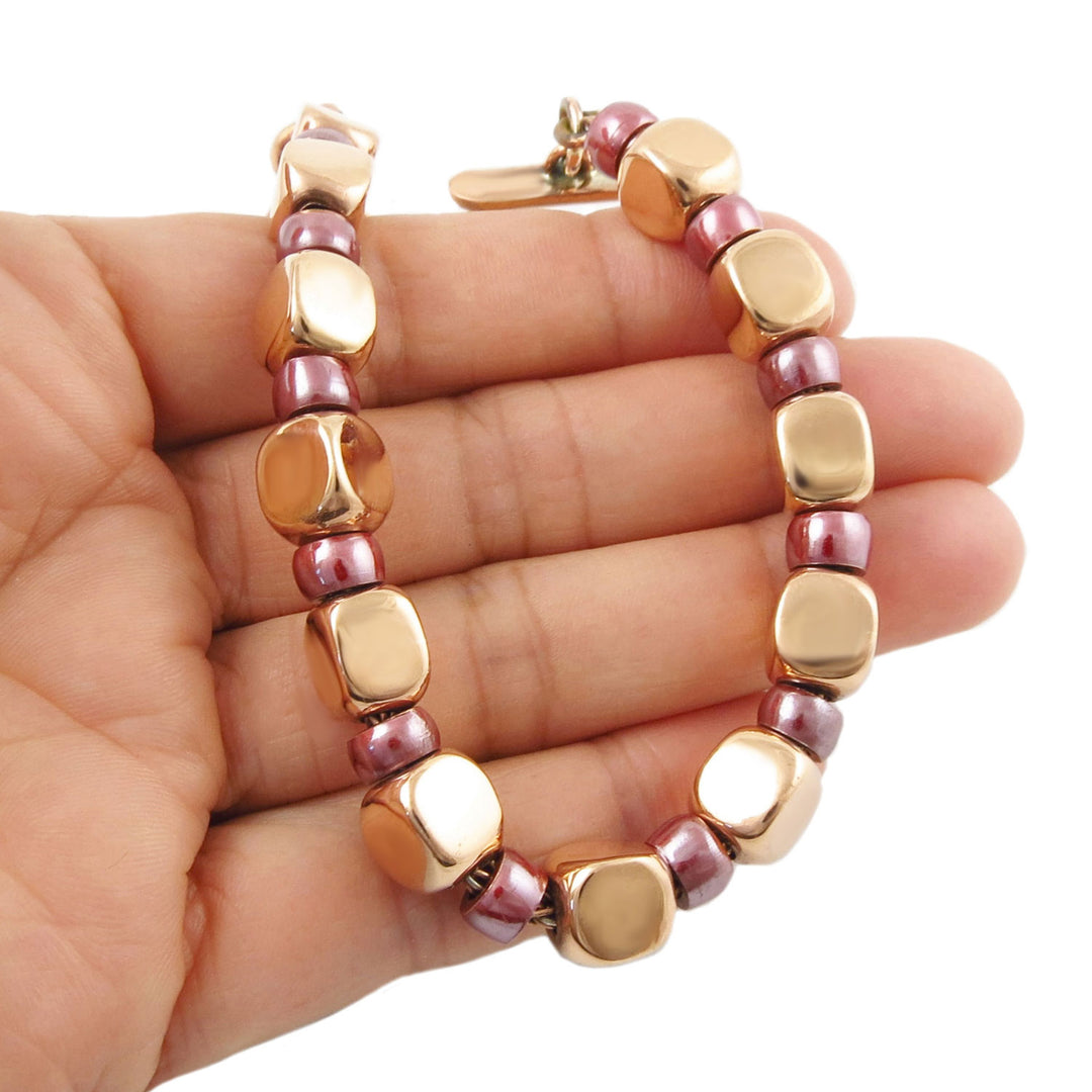 Beaded copper bracelet with polished square links and maroon spacer beads on a hand against a white background