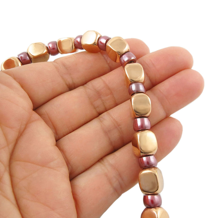 Beaded bracelet with polished copper links and maroon spacer beads on a hand against a white background