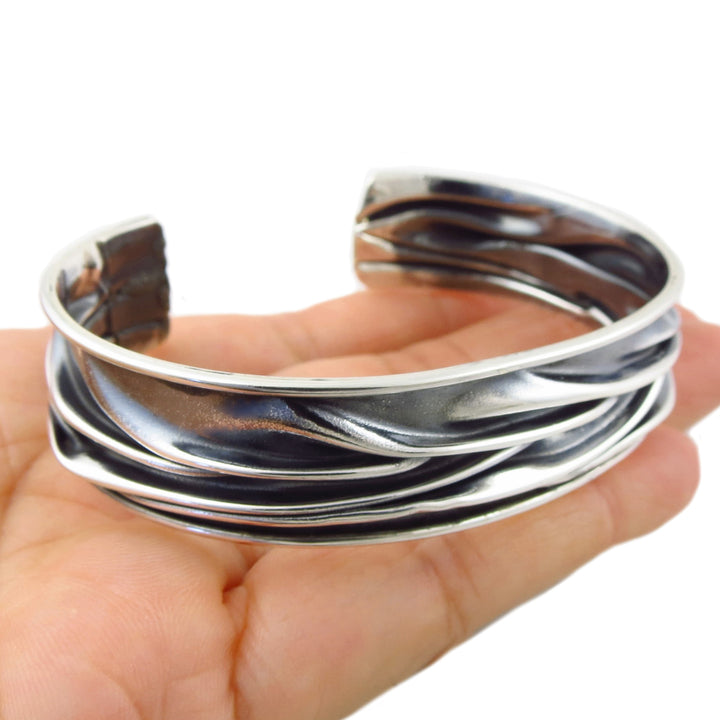 A polished and antiqued two tone sterling 925 silver cuff bracelet with a crushed and crumpled design, held in a woman's hand against a plain white background.