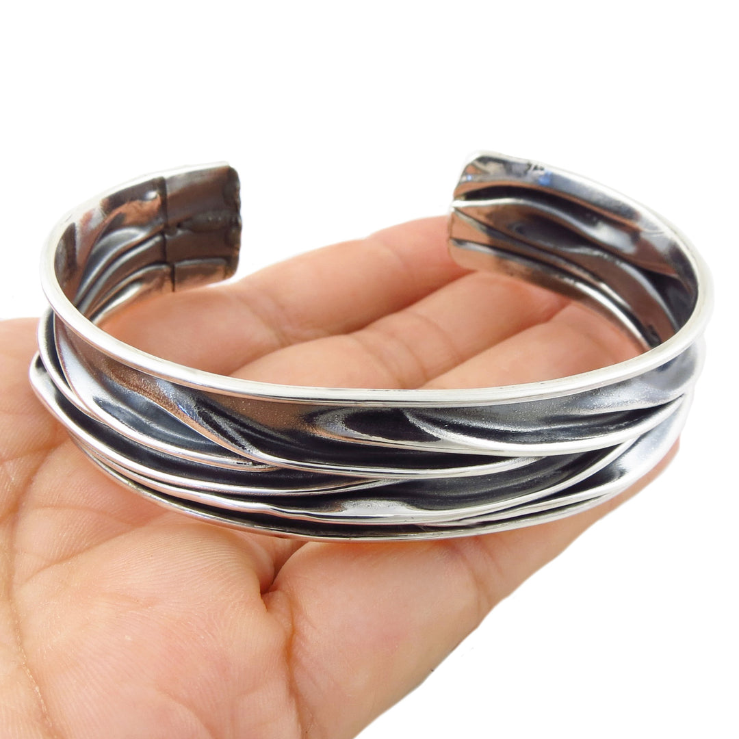 A polished and blackened antiqued Mexican 925 sterling silver cuff bracelet with a textured, crushed layered design, shown resting on a female hand against a white background. 