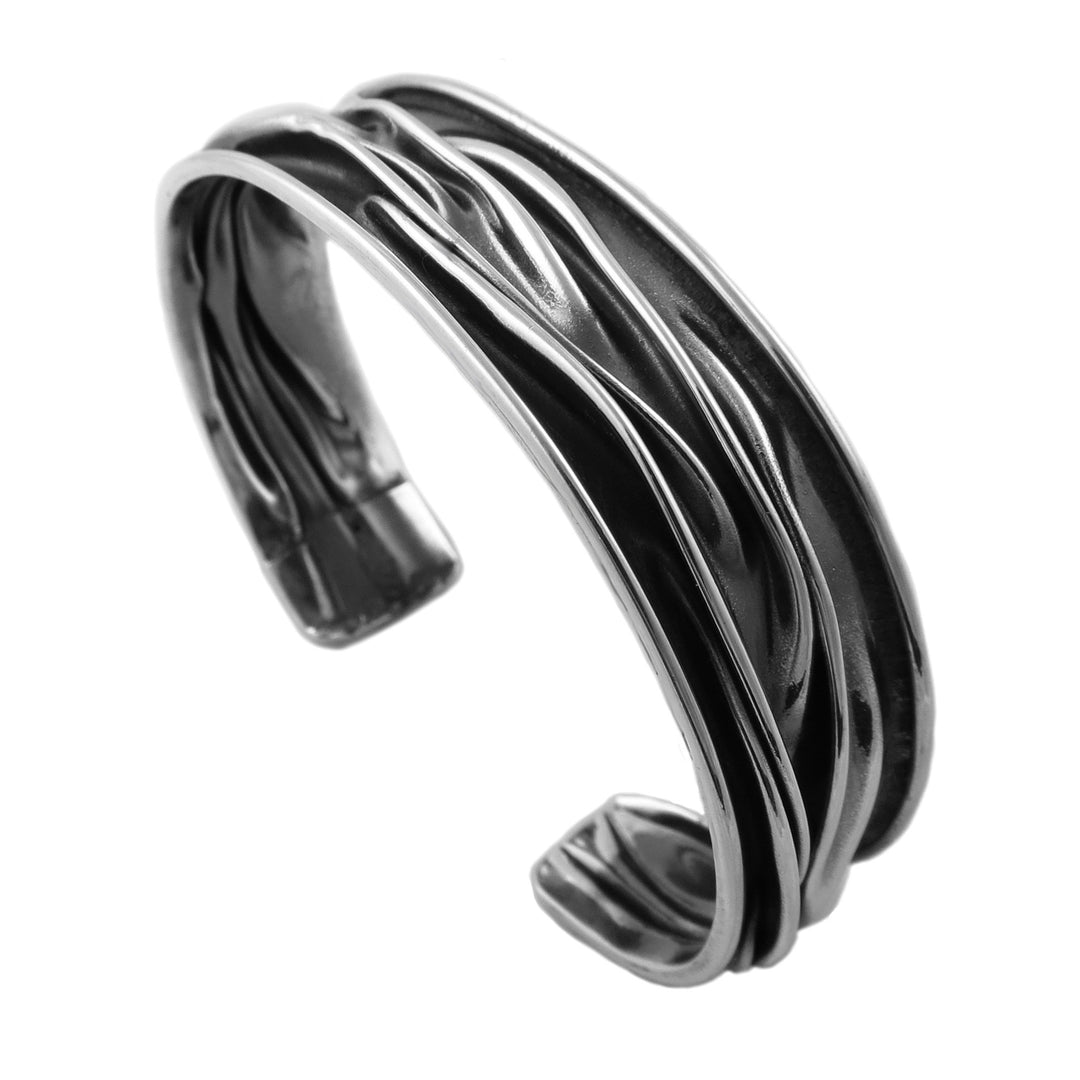 A polished and antiqued two tone UK hallmarked sterling 925 silver cuff bracelet with a crushed, layered design, shown on a plain white background.