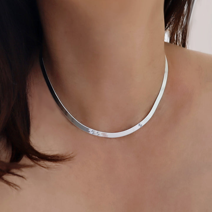 Flat silver snake chain necklace on a person's neck with a neutral background