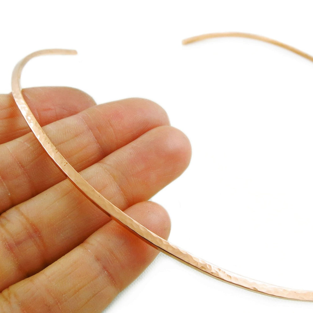 Hammered solid copper choker necklace held between fingers on a white background