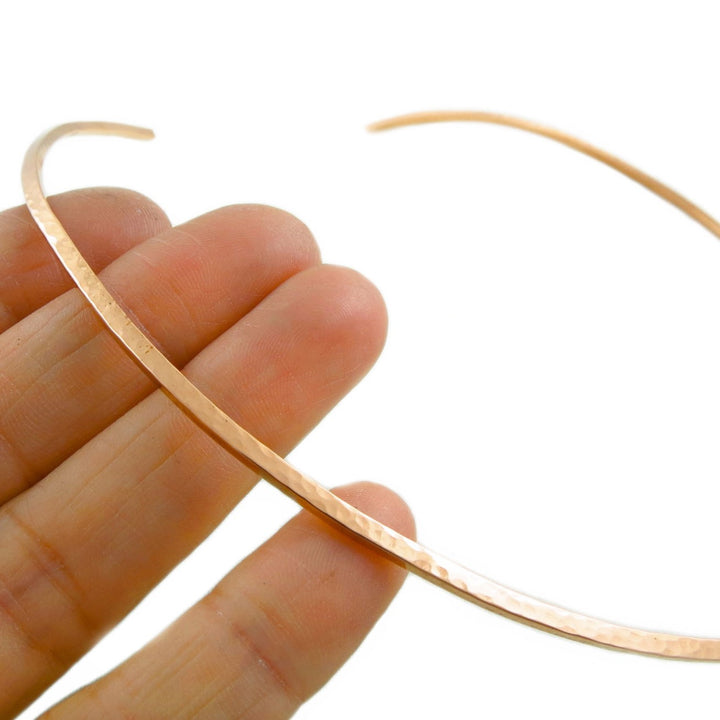 Hammered copper choker necklace held between fingers against a white background