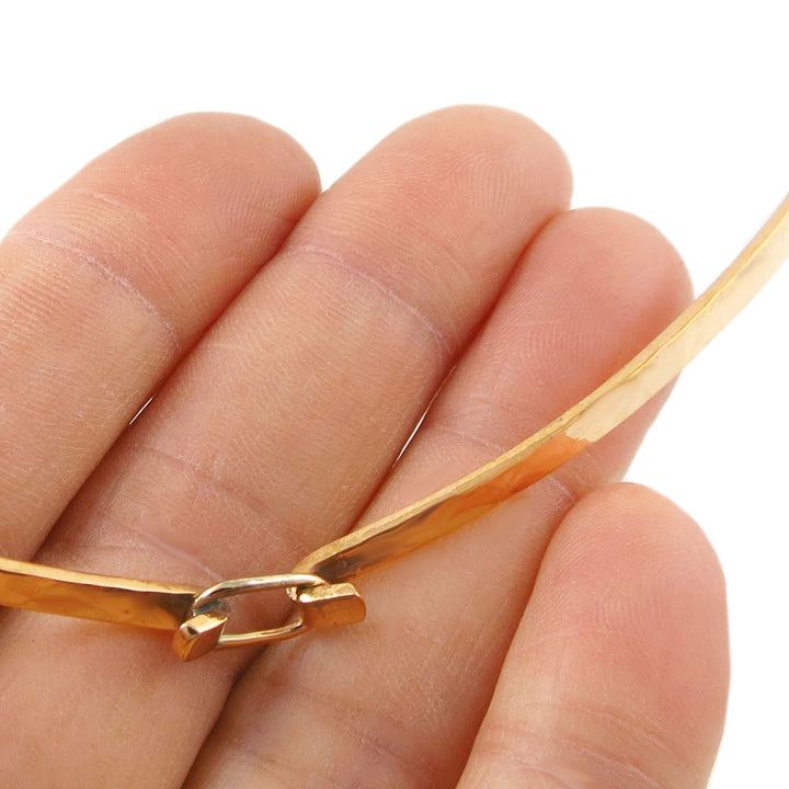 Ladies choker in hammered copper held between fingers on a white background