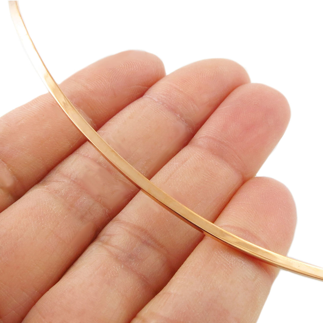 A solid polished copper necklace choker being held between fingers on a white background