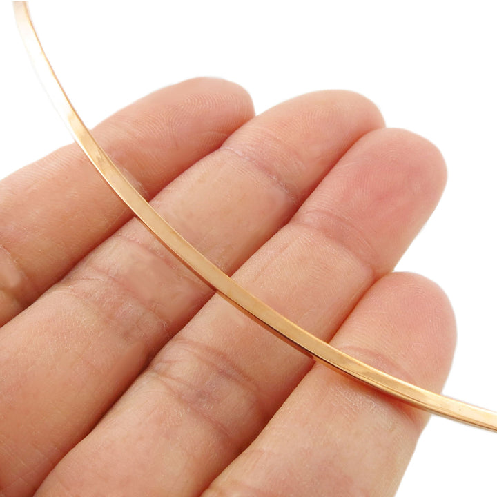 A solid polished copper necklace choker being held between fingers on a white background