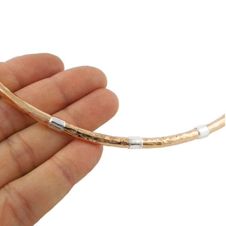 Woman's hand holding a hammered copper and silver rigid choker necklace on a white background