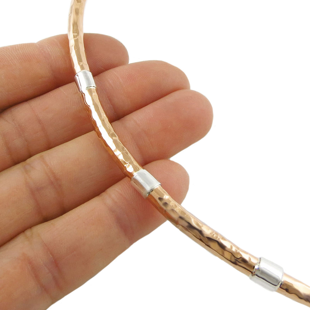 Copper and 925 silver rigid choker necklace for women held between fingers on a white background