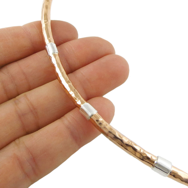 Copper and 925 silver rigid choker necklace for women held between fingers on a white background