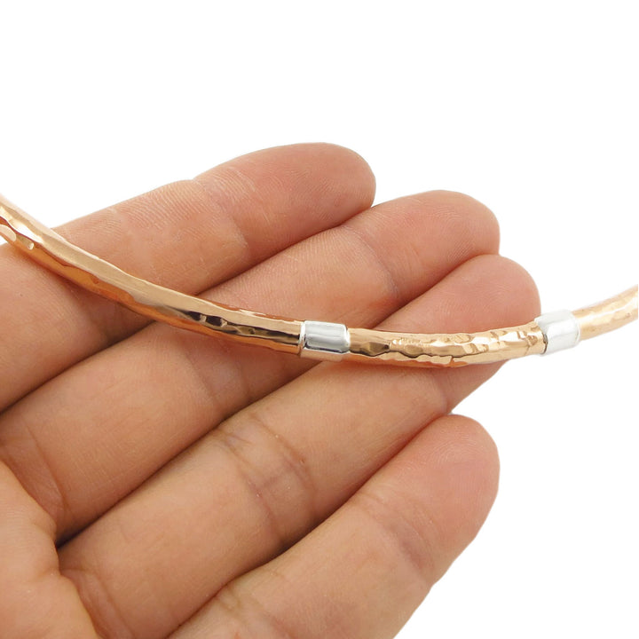 A solid hammered choker necklace with 925 silver accents held in a woman's hand against a white background