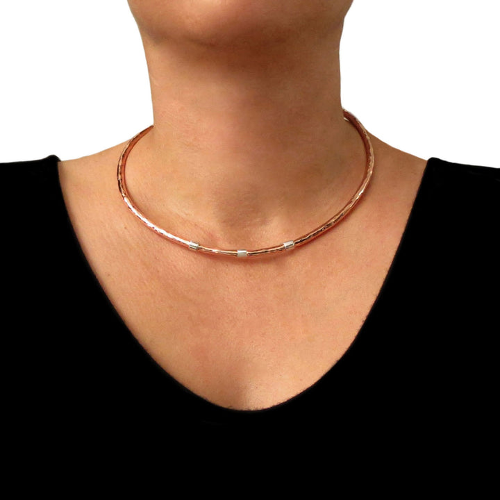 Large rigid hammered copper and 925 silver choker torque necklace worn by a woman wearing a black top against a white background
