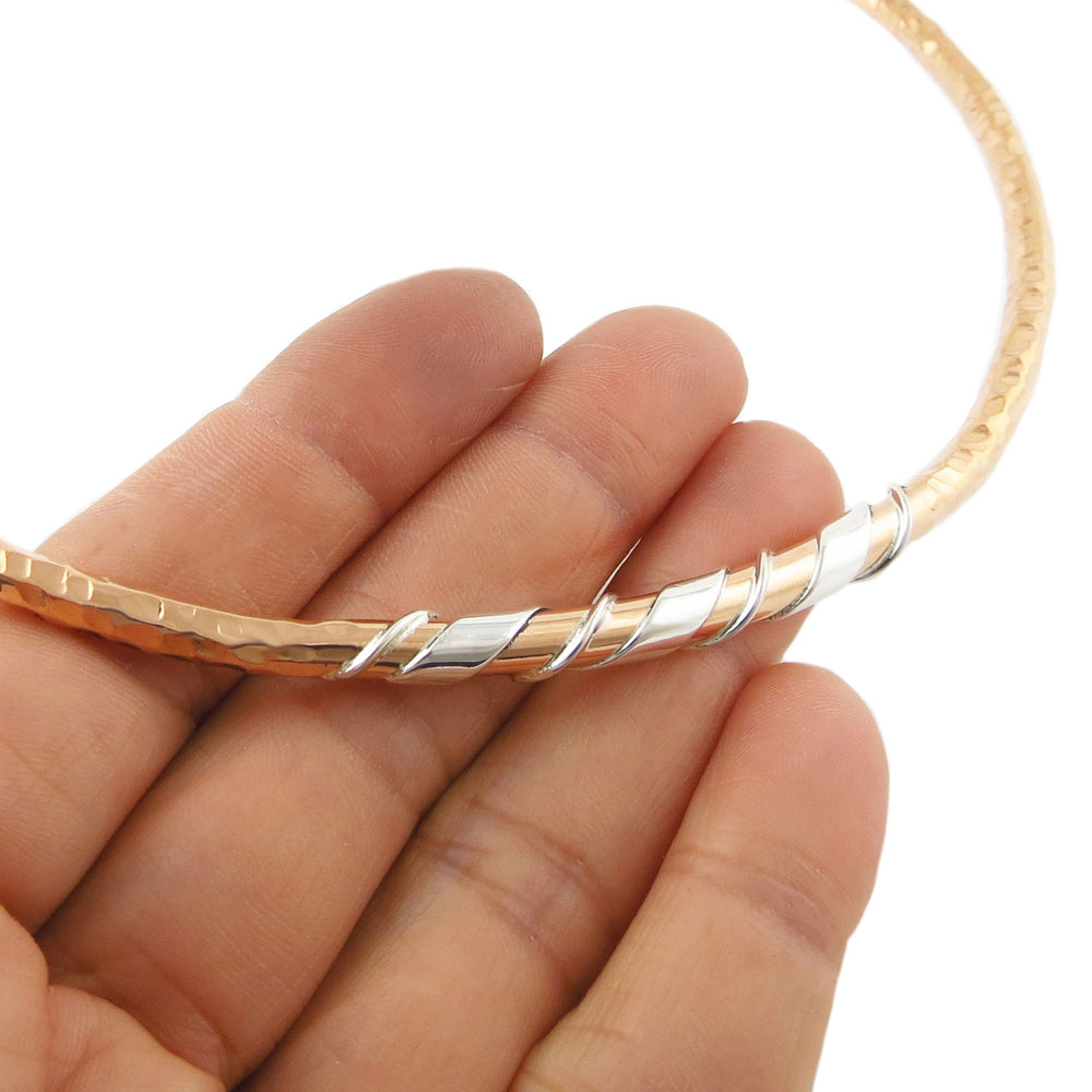 Rigid hammered copper and silver choker necklace for women held in a hand against a white background