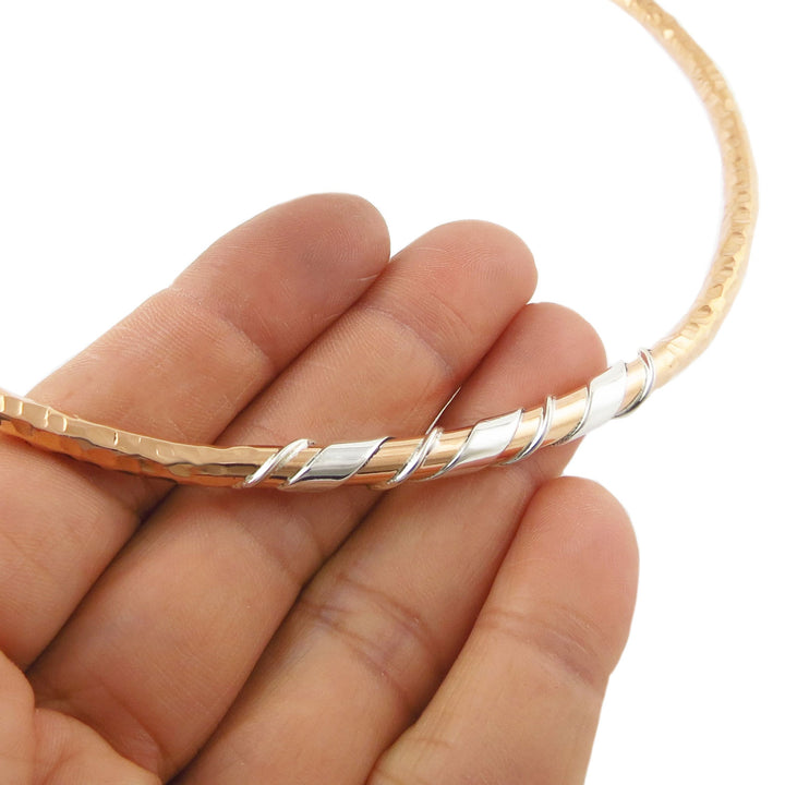 Rigid hammered copper and silver choker necklace for women held in a hand against a white background