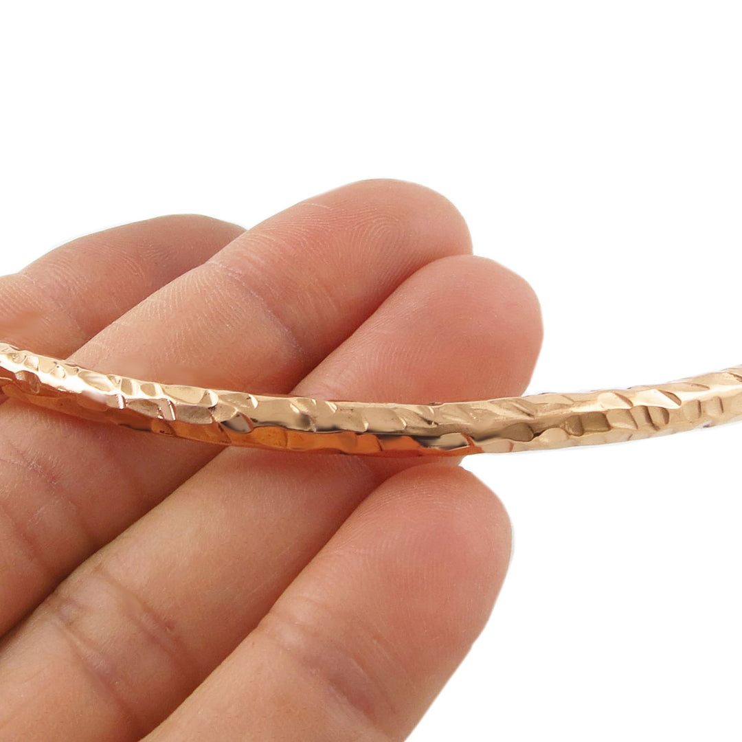 Hammered copper choker necklace held in a ewomna's hand on a white background. 