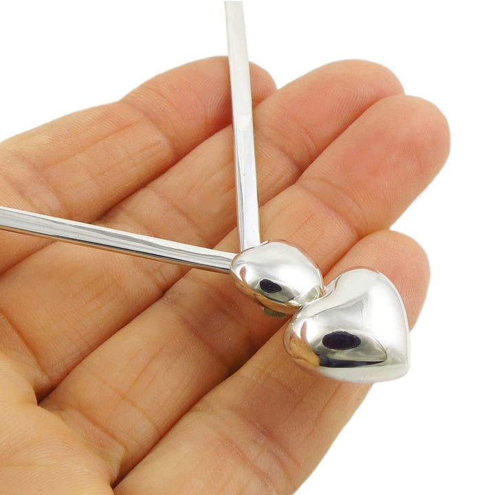A close-up of a polished silver choker necklace with heart-shaped accents held in n a woman's hand. 