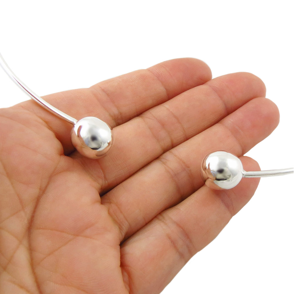 A close-up of a woman's hand holding a thin silver wire choker necklace with two polished spherical ball beads, shown against a plain white background.