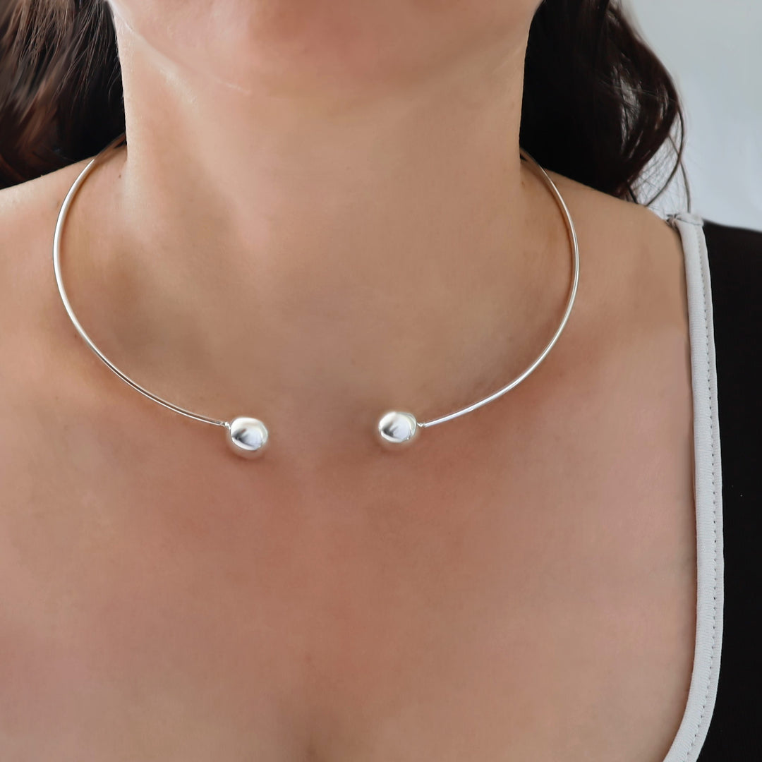 A close-up of a woman wearing a delicate sterling 925 silver open-circle choker necklace with two small polished bead  ends.